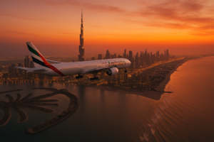 Voyage à Dubaï avec Emirates : un avion Emirates survolant Dubaï au coucher du soleil, avec la Burj Khalifa et les plages du golfe en arrière-plan.